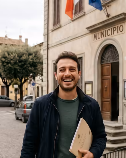 Young man smiling outside an Italian town hall with a folder of documents